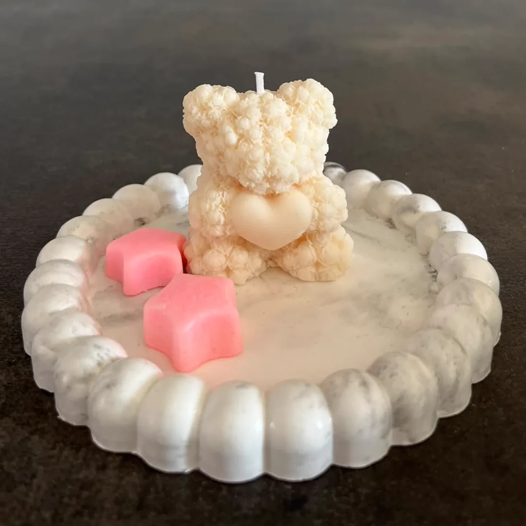 Estrellas de cera rosa junto a una vela de osito, sobre bandeja de yeso